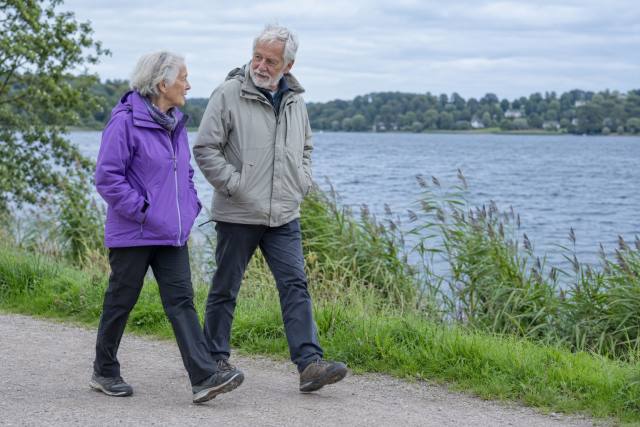 To fiktive ældre på en søsti, den ene i violet jakke; ikke konkrete ATP-medlemmer eller dokumentation af pensionsforhøjelsen. AI-genereret, fotorealistisk temabillede; viser ikke den konkrete begivenhed.
