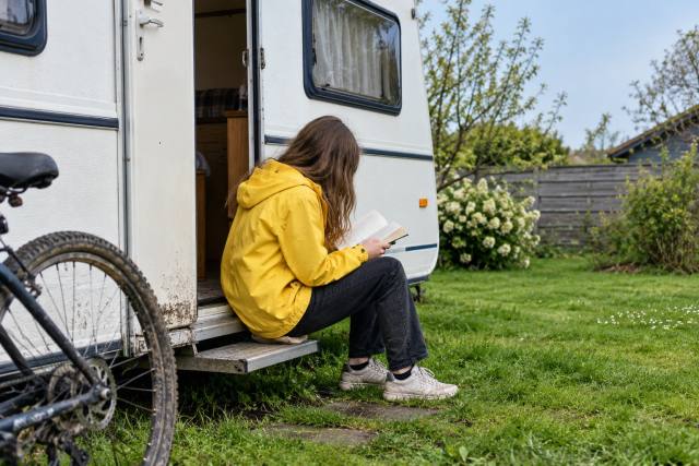Fiktiv ung læser i gul jakke ved en hvid campingvogn; ikke en af prisvinderne, et bestemt bogomslag eller dokumentation af prisuddelingen. AI-genereret, fotorealistisk temabillede; viser ikke den konkrete begivenhed.
