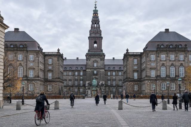 AI-genereret, fotorealistisk temabillede af Christiansborg med cykler og anonyme forbipasserende; ikke et fotografi eller dokumentation af en konkret politisk begivenhed eller statistikoffentliggørelse.