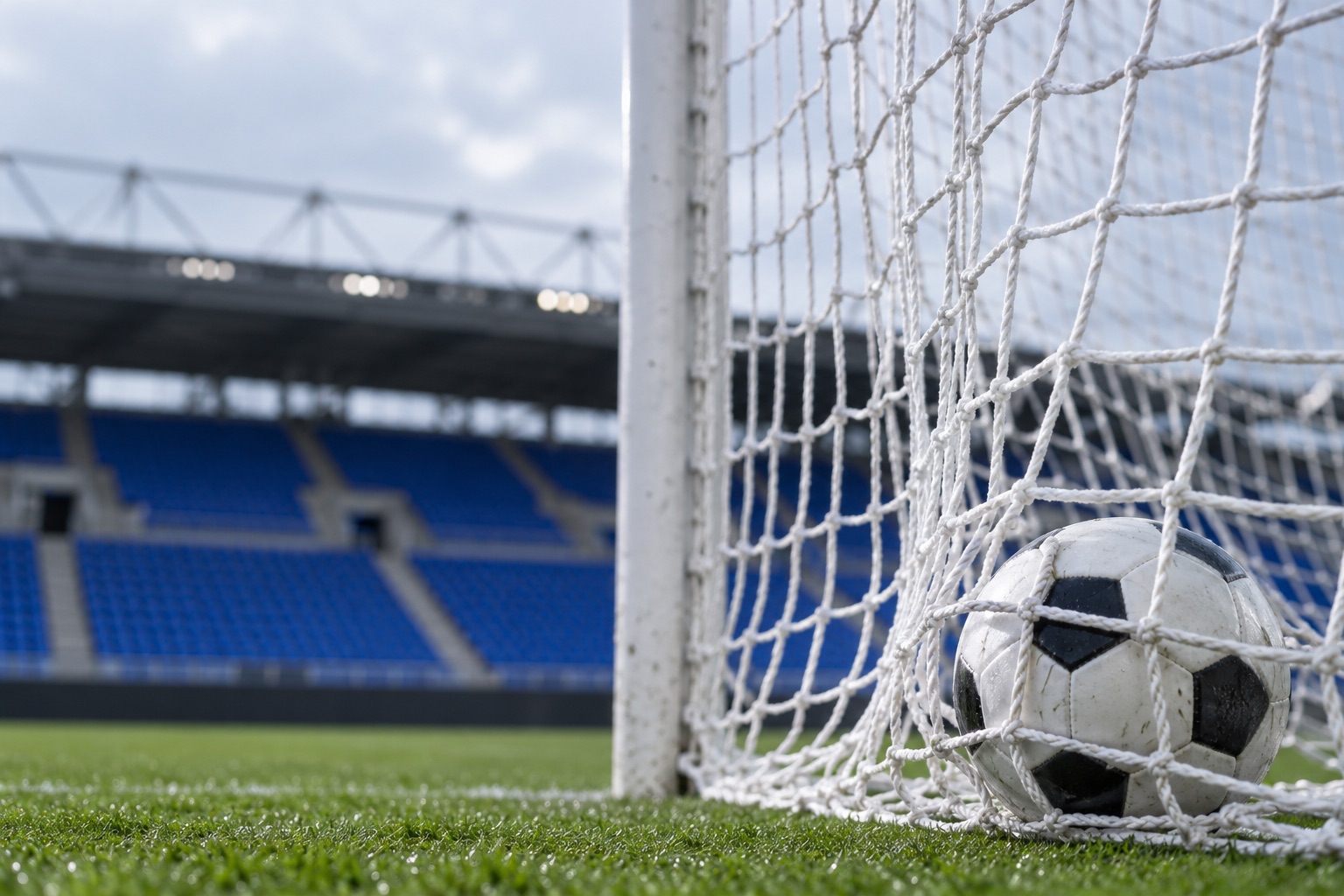 Fodbold i et hvidt målnet med blå tribuner i køligt dagslys på et fiktivt stadion; ikke et foto fra FCK-kampen i Beograd. AI-genereret, fotorealistisk temabillede; viser ikke den konkrete begivenhed.