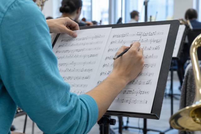 Hænder retter et fiktivt orkesterpartitur ved en prøve; ikke John Williams, Bernard Herrmann eller dokumentation af prisuddelingen. AI-genereret, fotorealistisk temabillede; viser ikke den konkrete begivenhed.